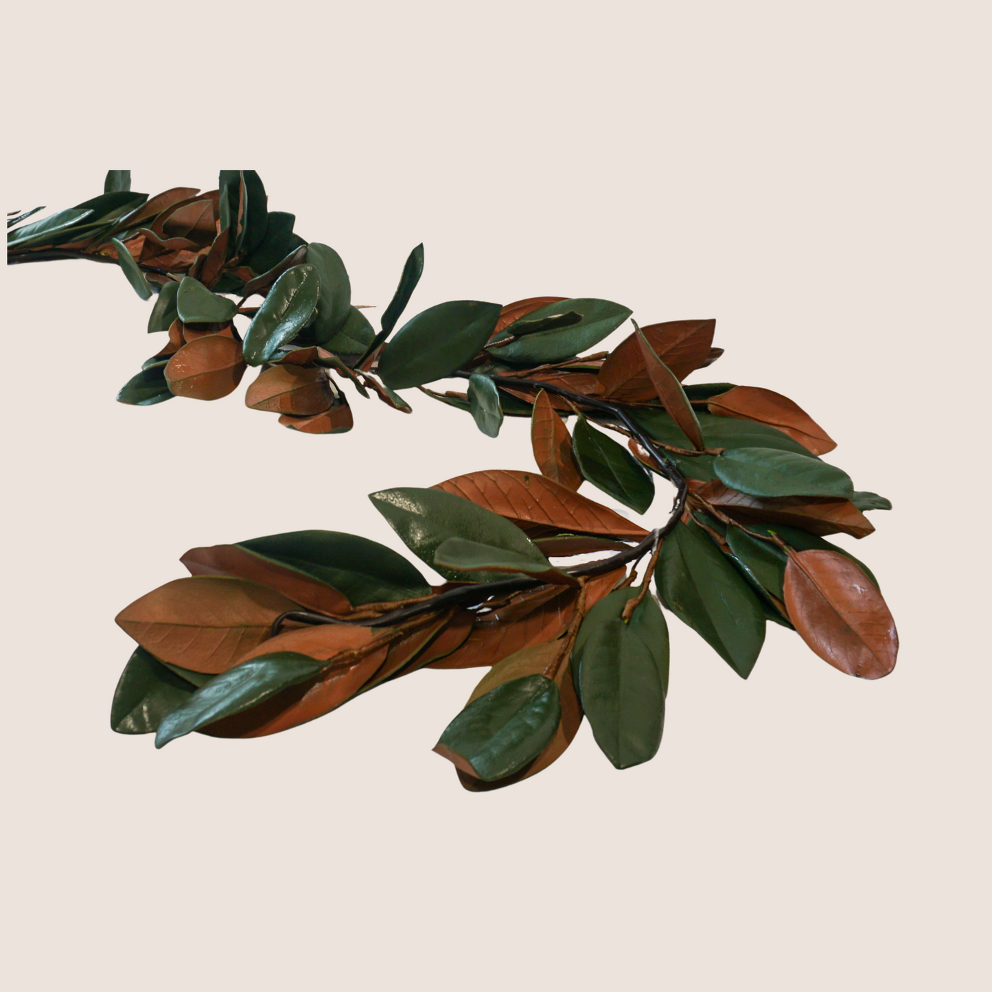 Artificial magnolia leaf garland with dark green and brown leaves against blush pink backdrop.