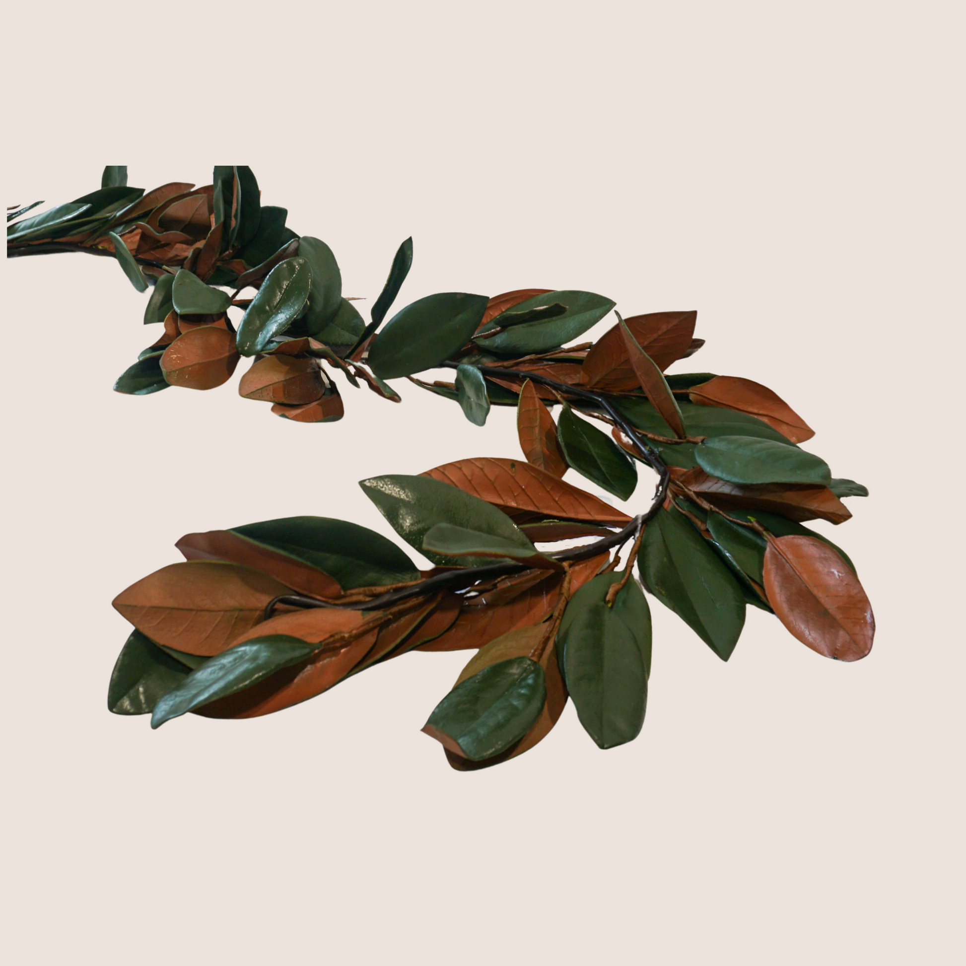 Artificial magnolia leaf garland with dark green and brown leaves against blush pink backdrop.