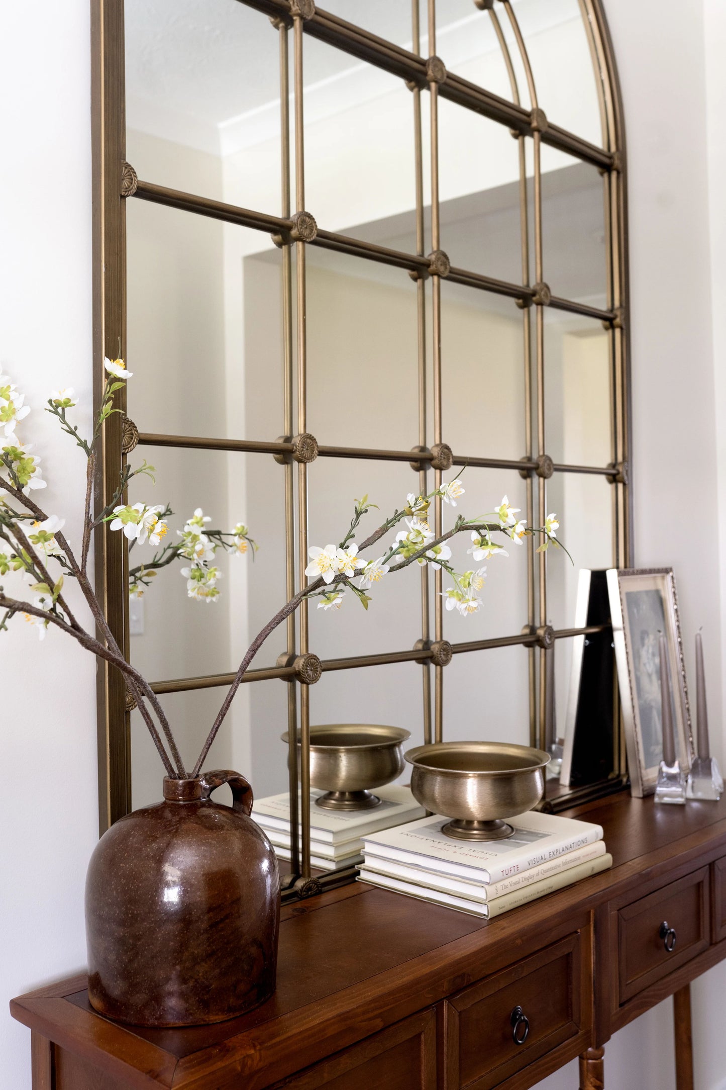 Artificial cherry blossom branch with budding flowers in white and yellow, styled in antique water jug. 