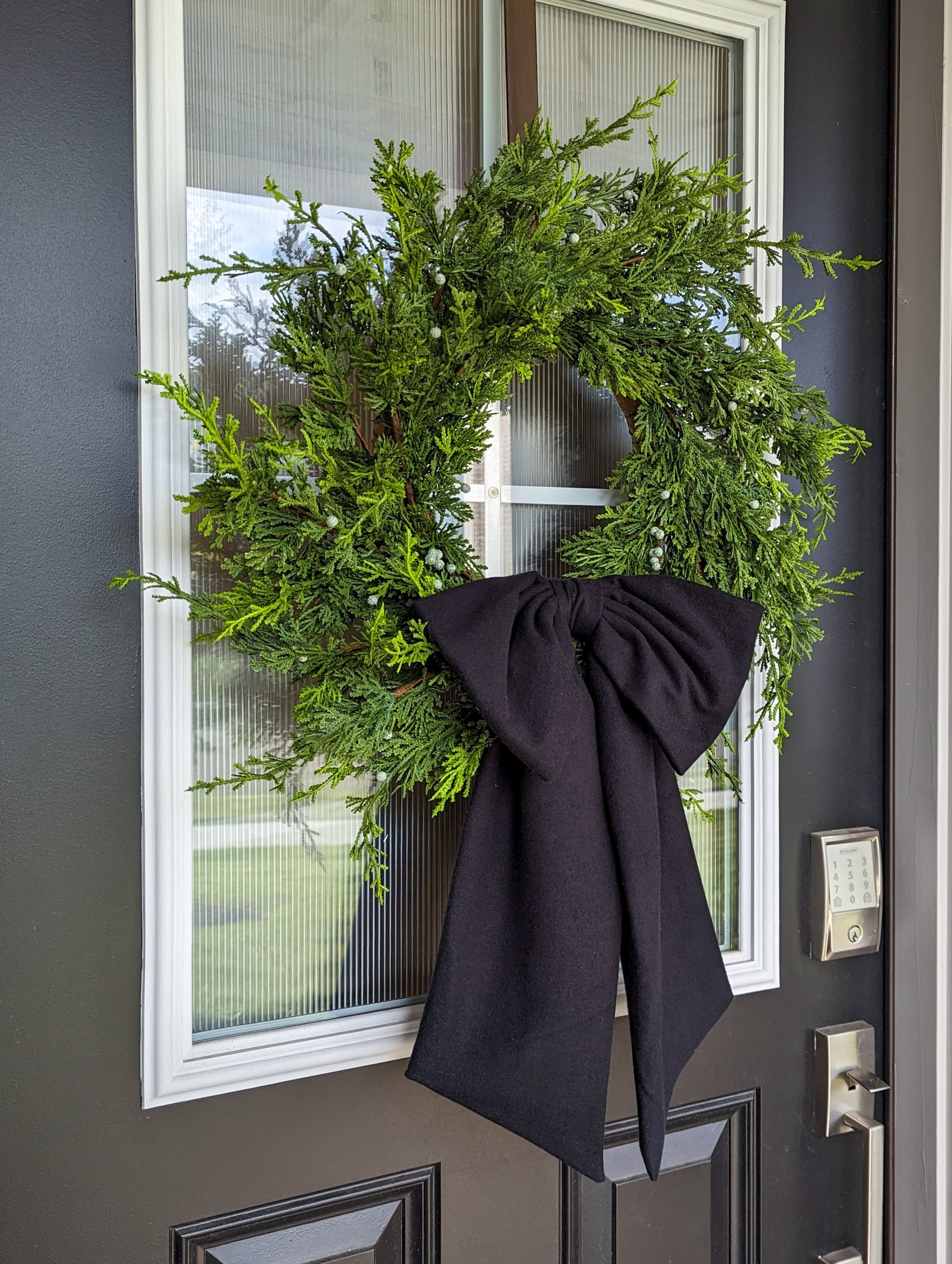 Soft black droopy fleece bow on juniper wreath for Christmas home decor.