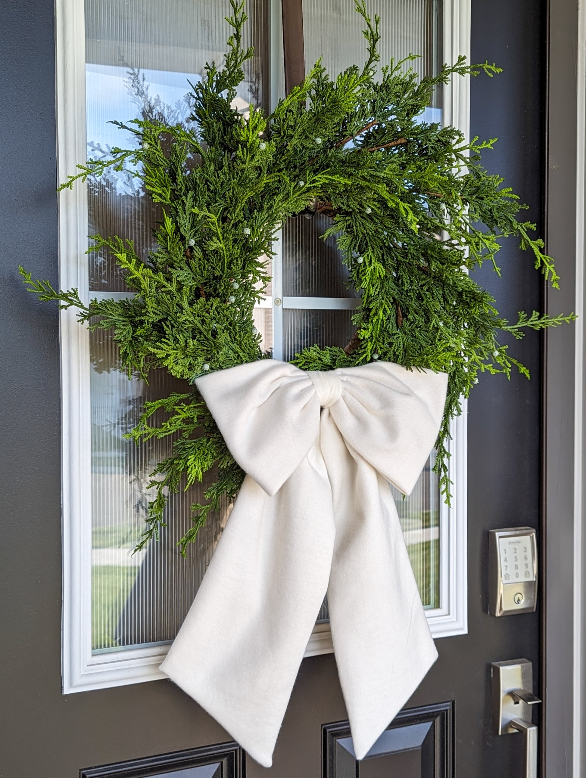 Cream white droopy fleece bow on juniper wreath for Christmas home decor.