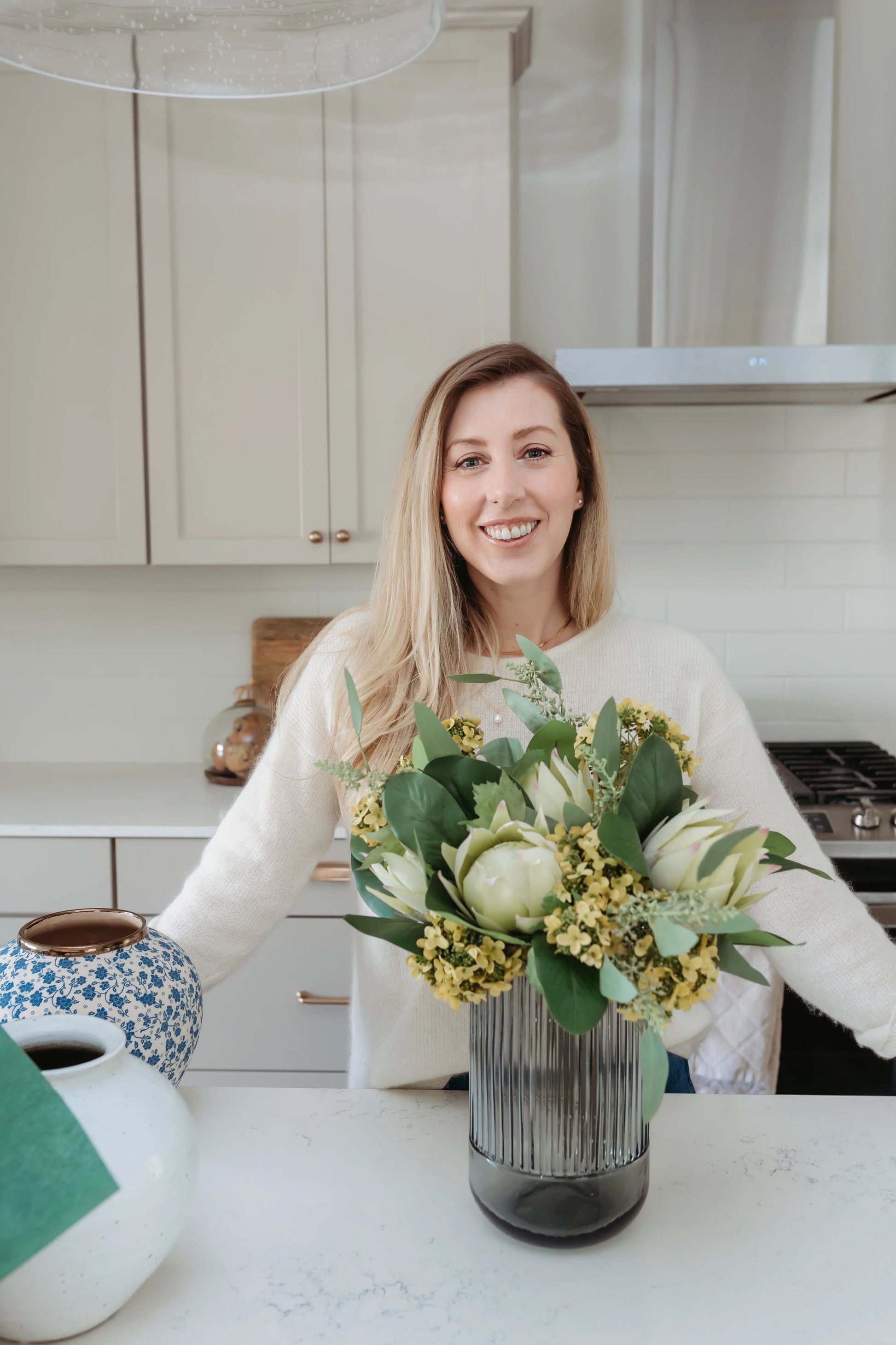Gray fluted vase being styled with summer arrangement of artificial flowers in kitchen.
