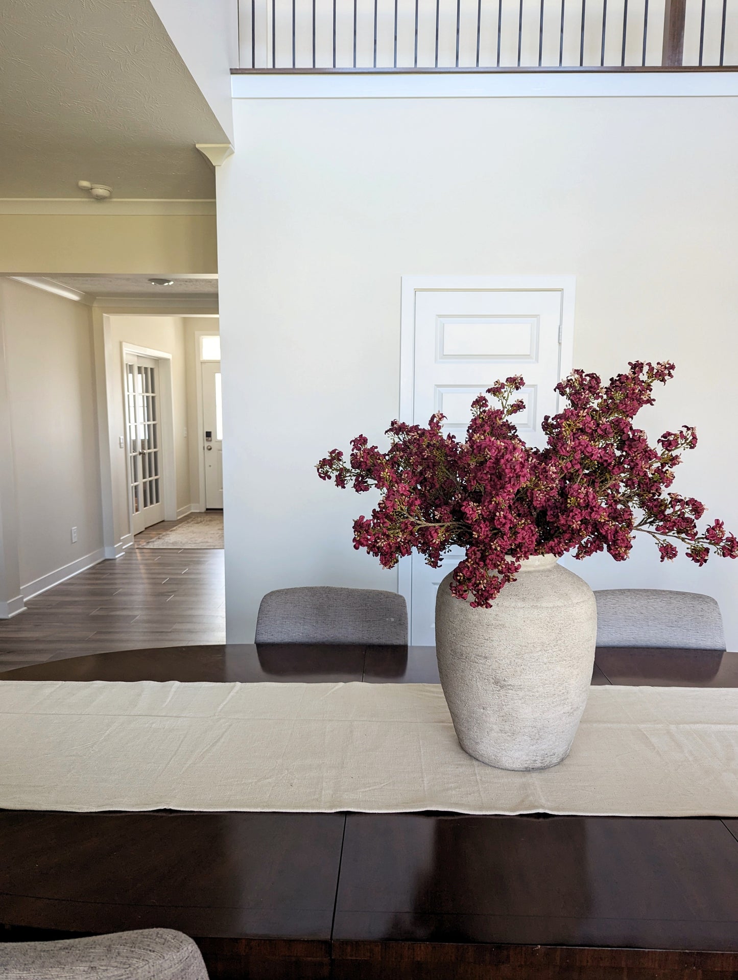 Bundle of artificial fall stems in dark pink, on wooden table in a beige vase.