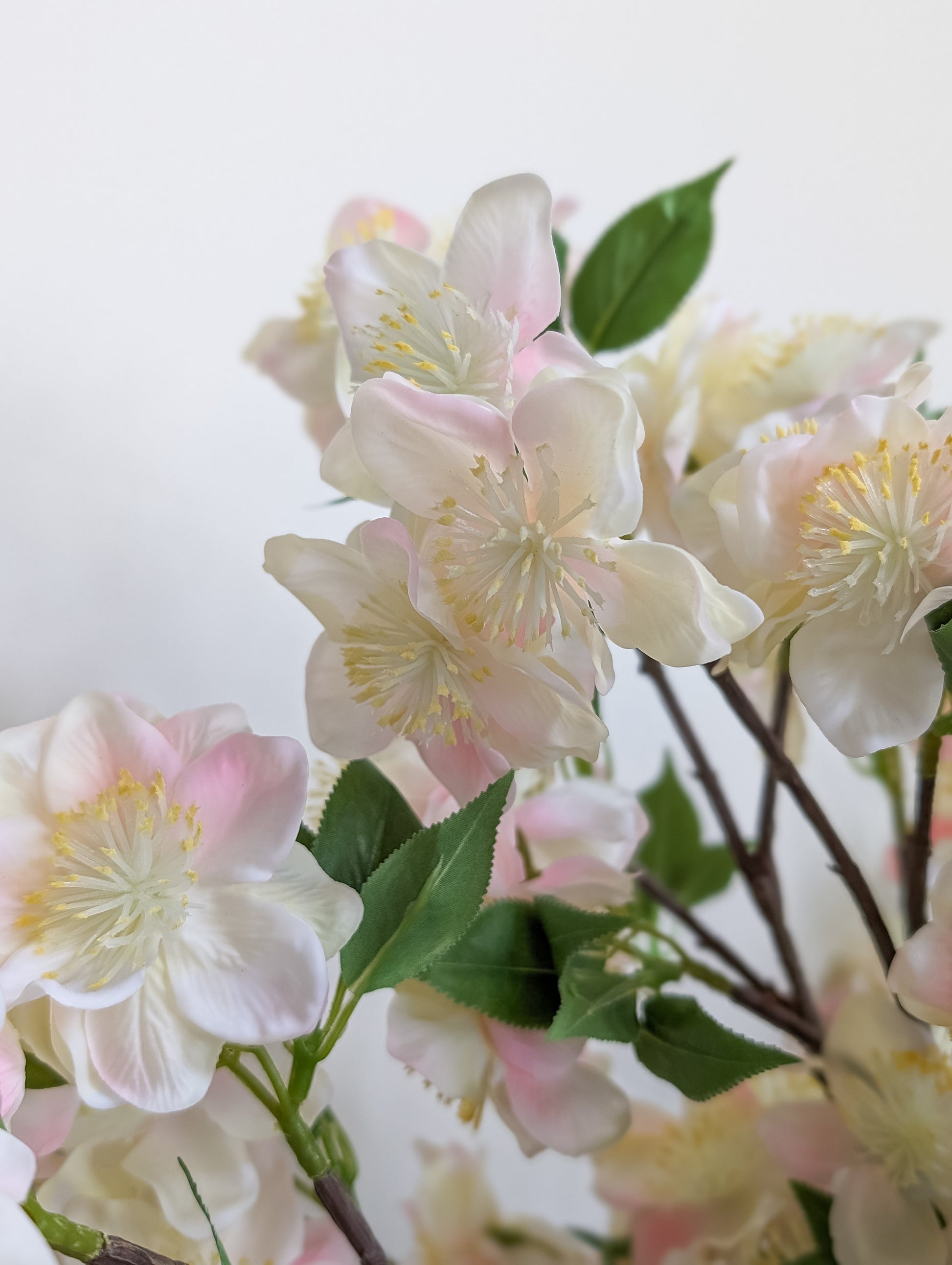 Close up of realistic faux cherry blossom stem with real touch petals with gradient of pink and white petals