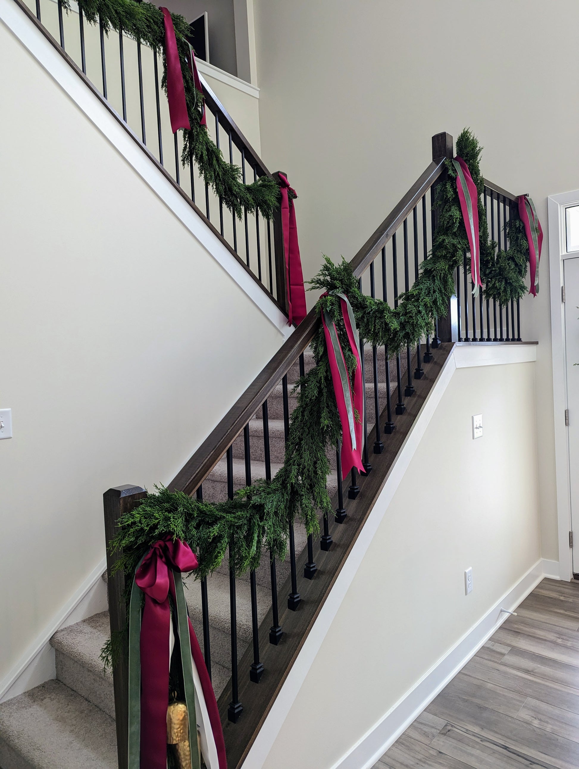 Faux greenery holiday Christmas garlands on stairs with green and red ribbon.