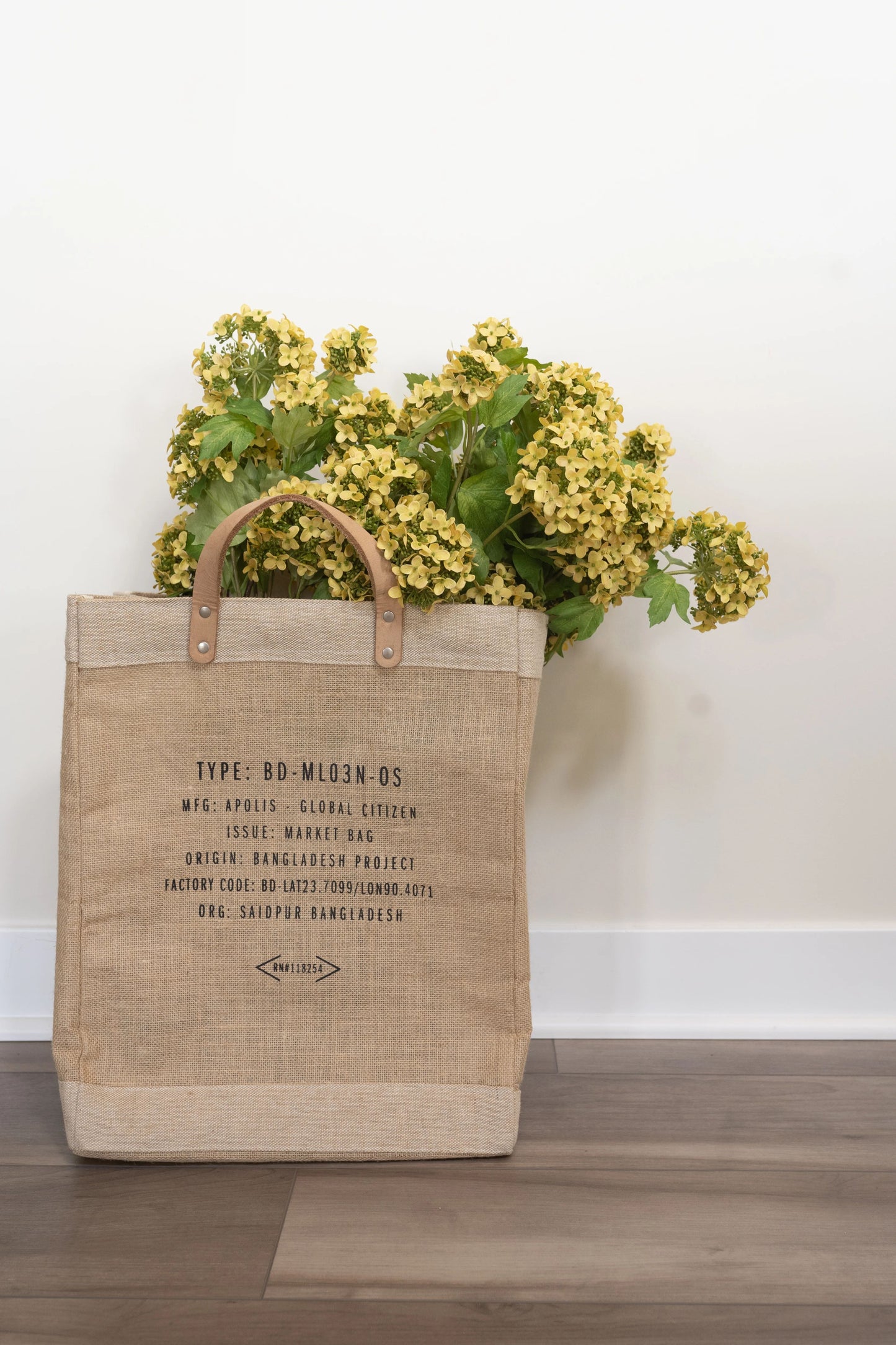 Bouquet of tall yellow snowball hydrangea stems in a rustic market tote against a white wall. 