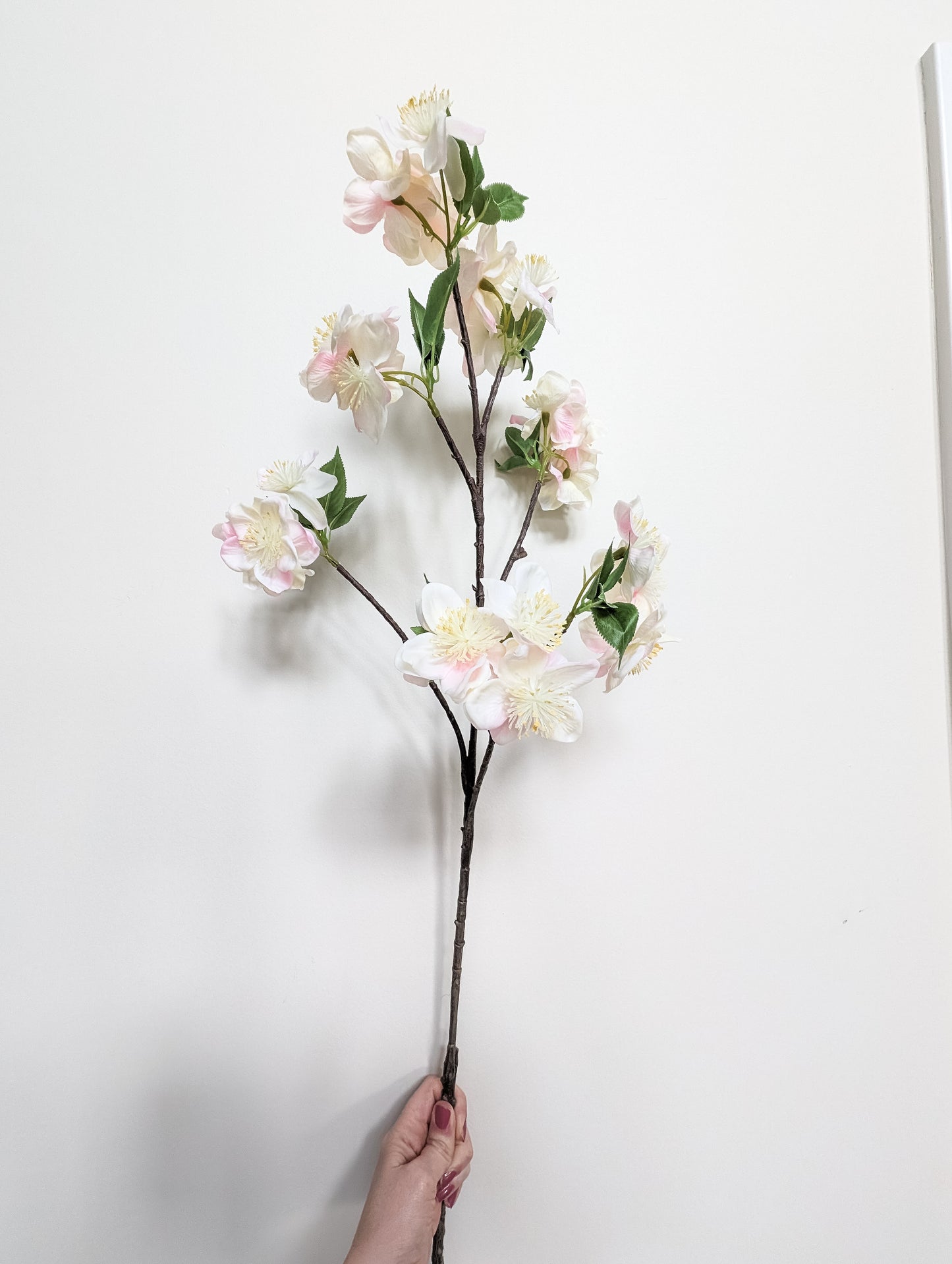 Life-like artificial cherry blossom stem with real touch petals with gradient of pink and white petals against white background.