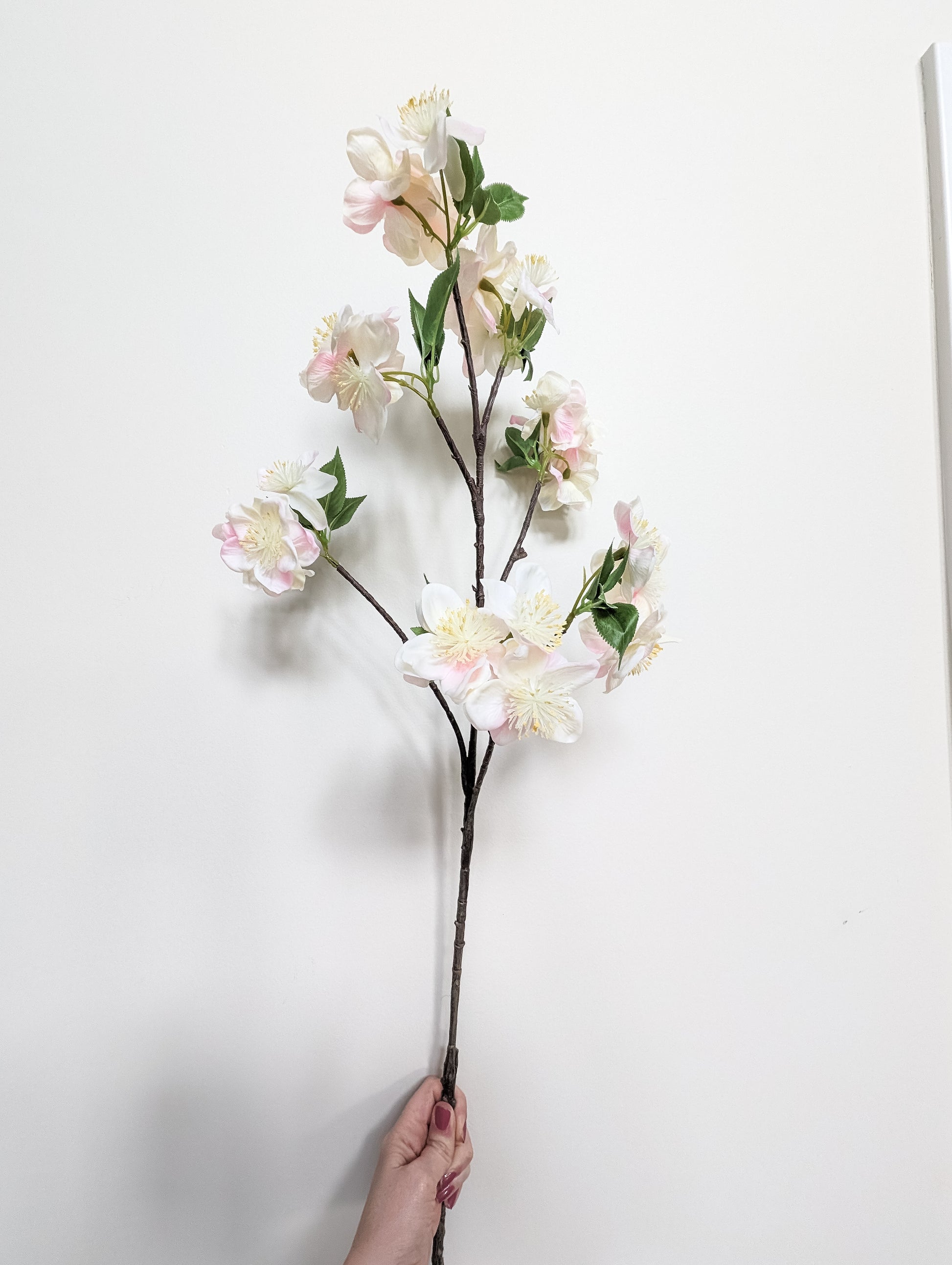 Life-like artificial cherry blossom stem with real touch petals with gradient of pink and white petals against white background.