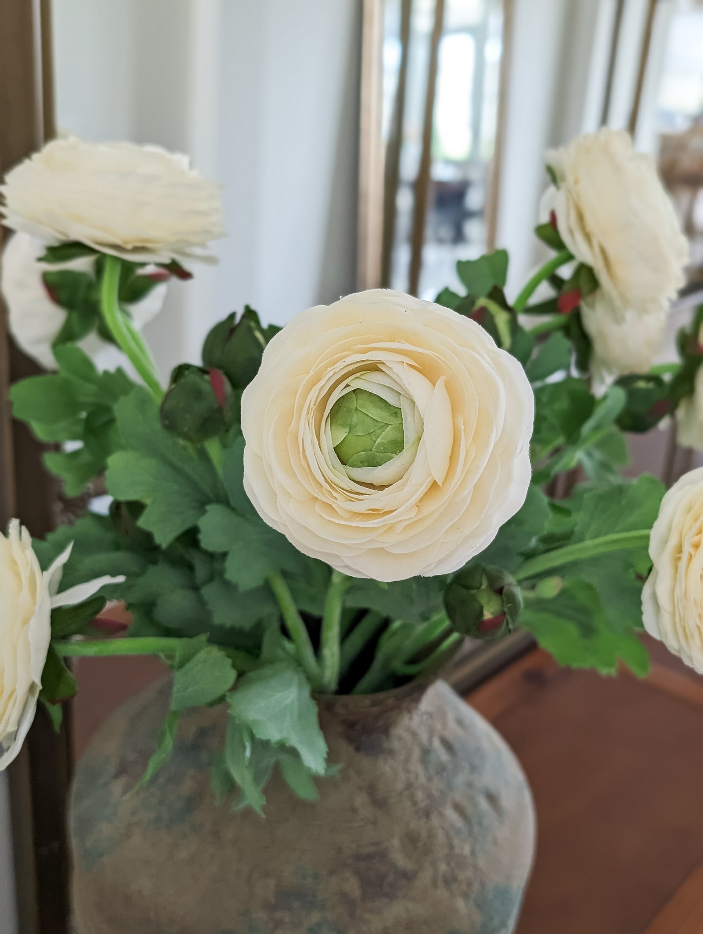 Close up of set of 6 artificial real touch blooming ranunculus flower in ivory, styled in vintage terra cotta vase against mirror.
