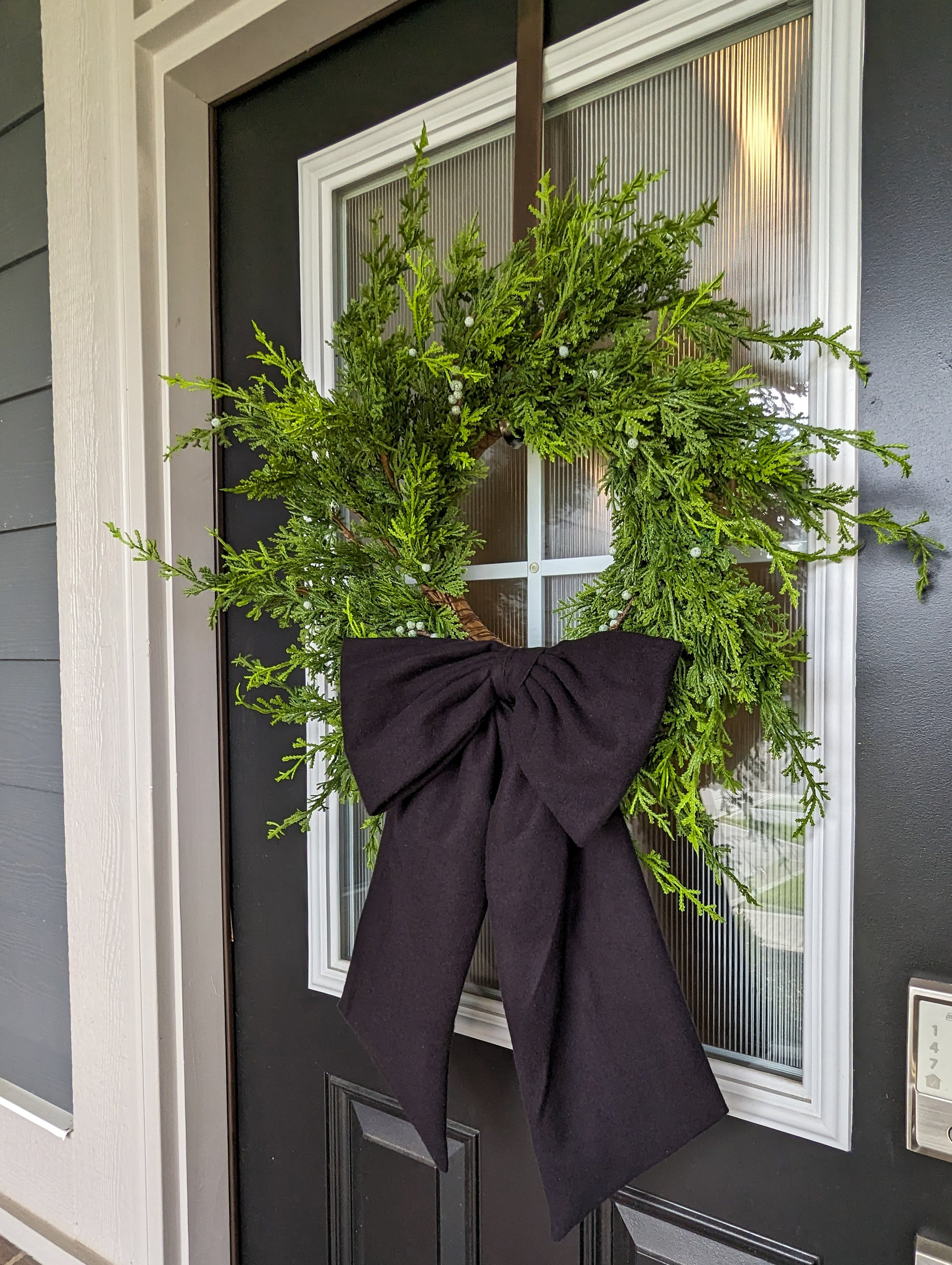 Black droopy fleece bow on juniper wreath for holiday home decorating.