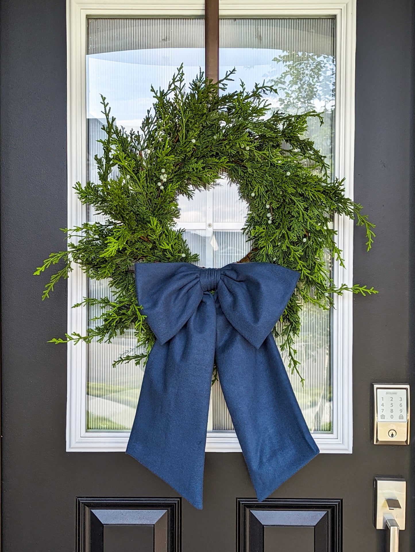 Navy blue droopy fleece bow on juniper wreath for holiday home decorating.