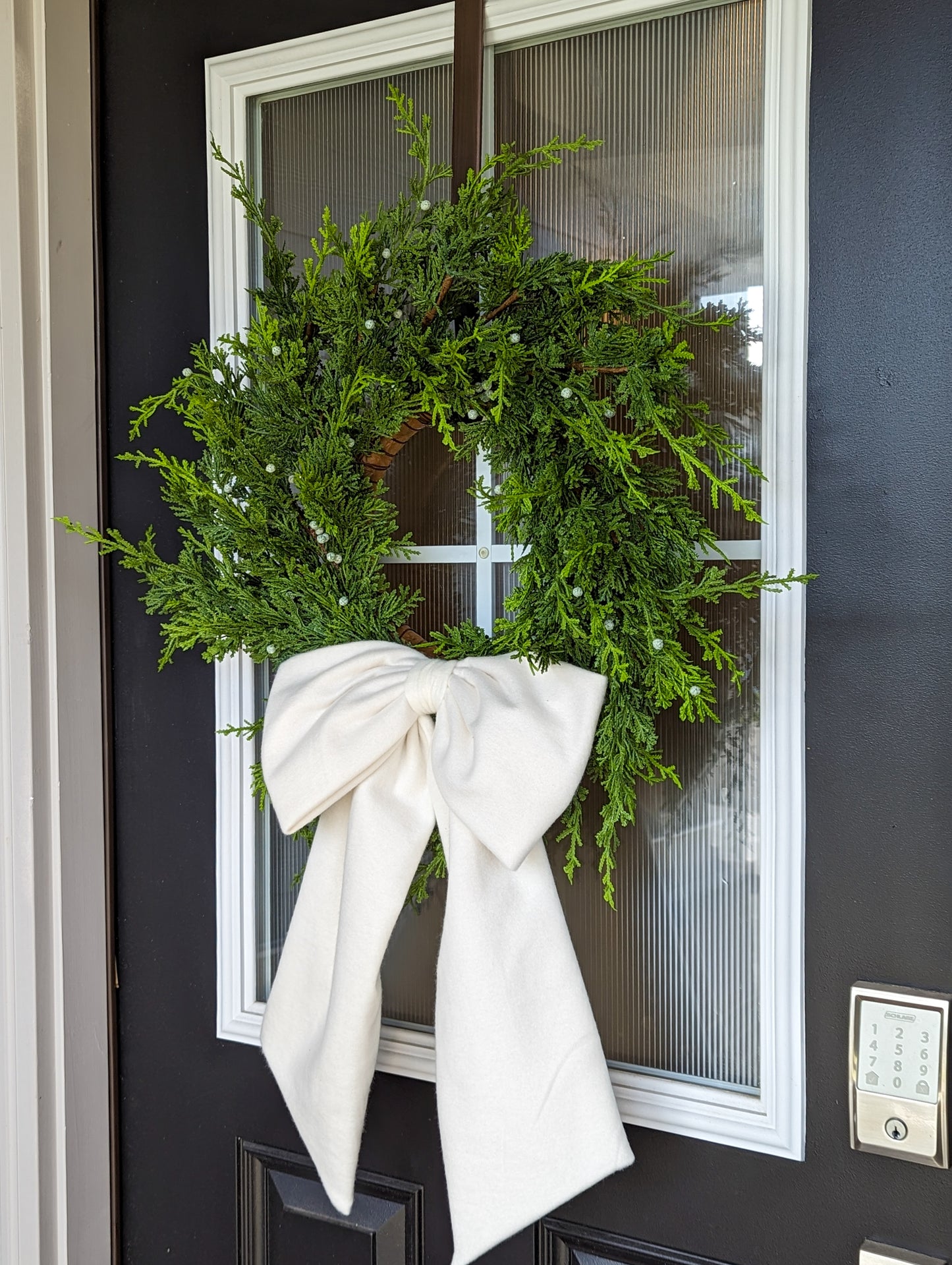 Ivory droopy fleece bow on juniper wreath for holiday front door decoration.