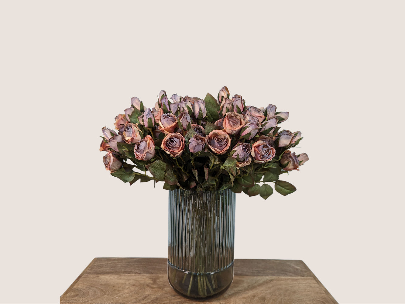 Image of a 9.5 inch tall fluted vase, bottom 1/4 of the vase is smooth glass, top 3/4 is fluted glass. Smokey grey in color. Against a neutral beige backdrop, featuring a bouquet of 5 cream white real touch hydrangeas and a separate vase with artificial dark mauve pink preserved dried roses.