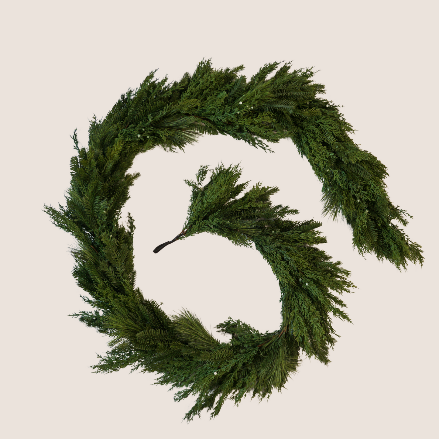 Lifelike Christmas garland comprised of a mixed of evergreen varieties including juniper, cedar, balsam fir, and ponderosa pine. 9 ft long garland coiled against a blush backdrop.