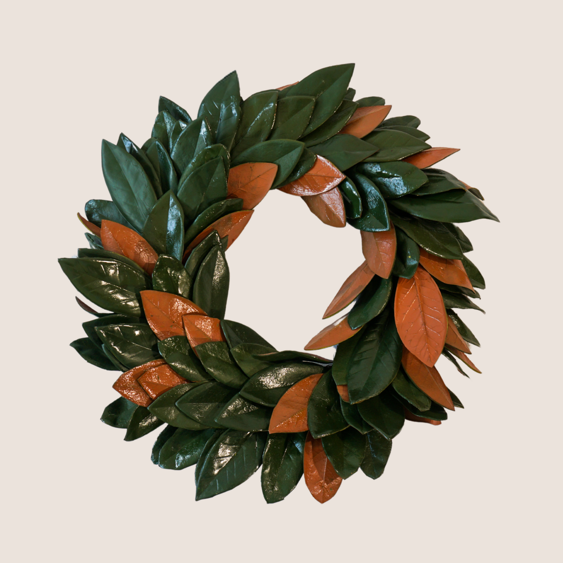 Artificial magnolia wreath pictured against blush backdrop. Extra full with mix of glossy green and brown leaves.