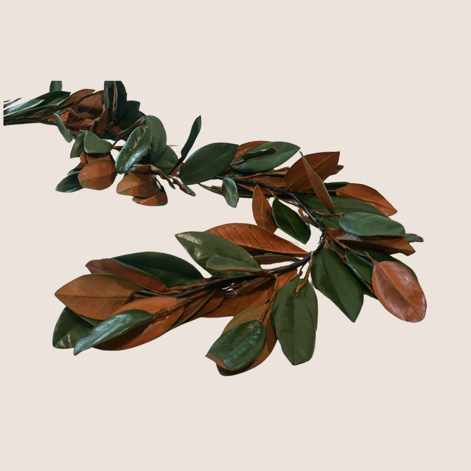 Artificial magnolia leaf garland with dark green and brown leaves against blush pink backdrop. 