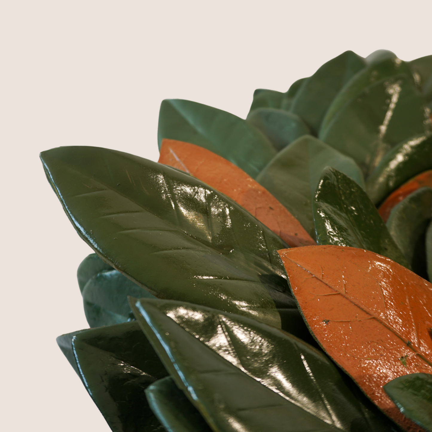 Close up of artificial magnolia wreath pictured against blush backdrop. Extra full with mix of glossy green and brown leaves.