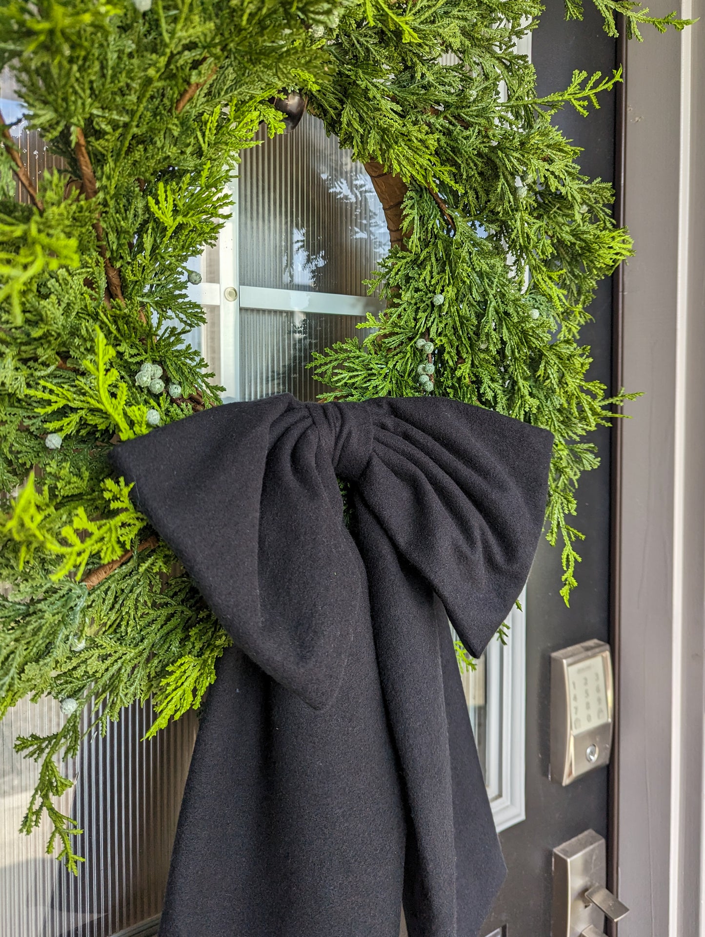 Black droopy fleece bow on juniper wreath for holiday front door decoration. 