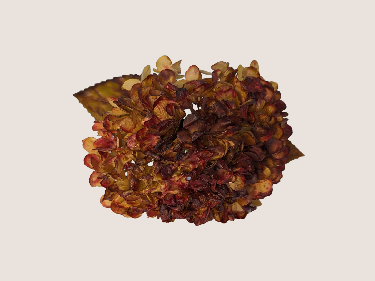 Close up of artificial fall hydrangea flower with red, brown, yellow, and green petals with gradient color against a light beige background showcasing realistic look dried florals and leaves.