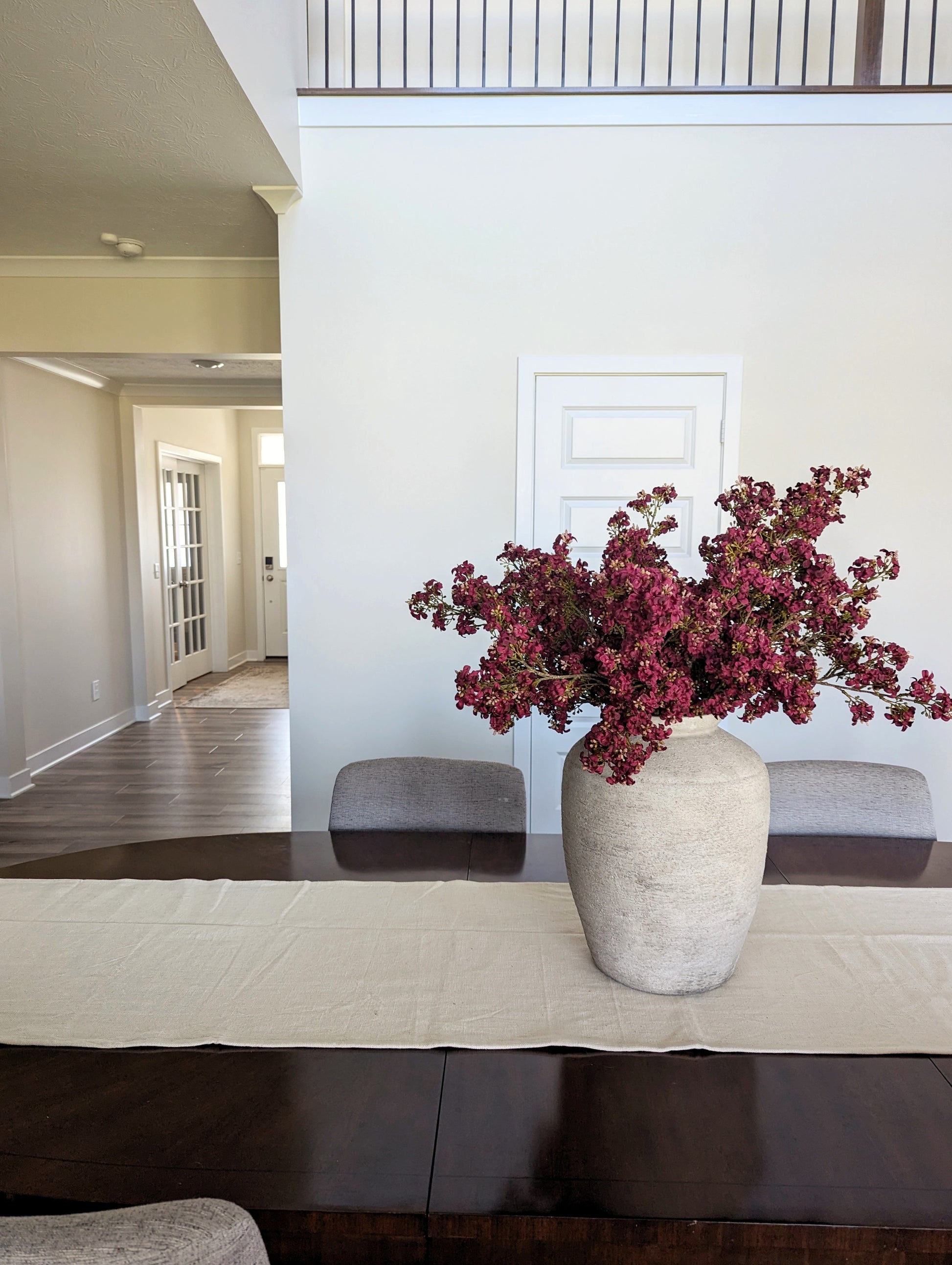 Bundle of artificial fall stems in dark pink, on wooden table in a beige vase. 