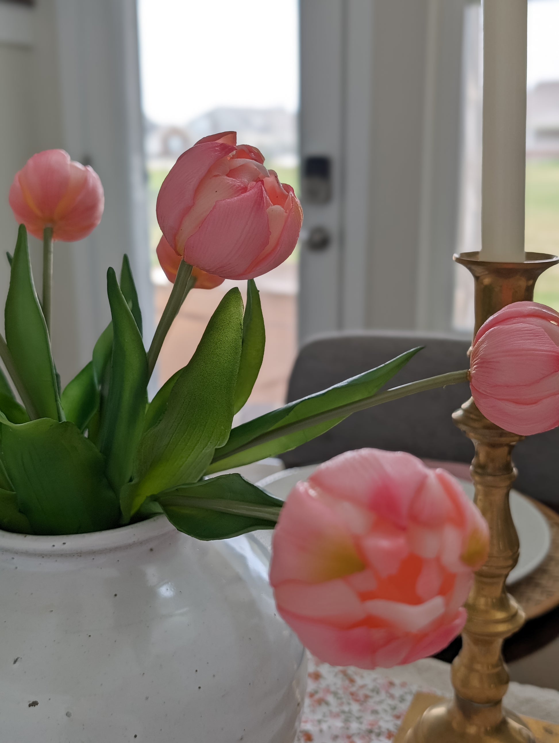 Close up of artificial pink tulips in  a bouquet styled in white vase set as part of spring tablescape. 