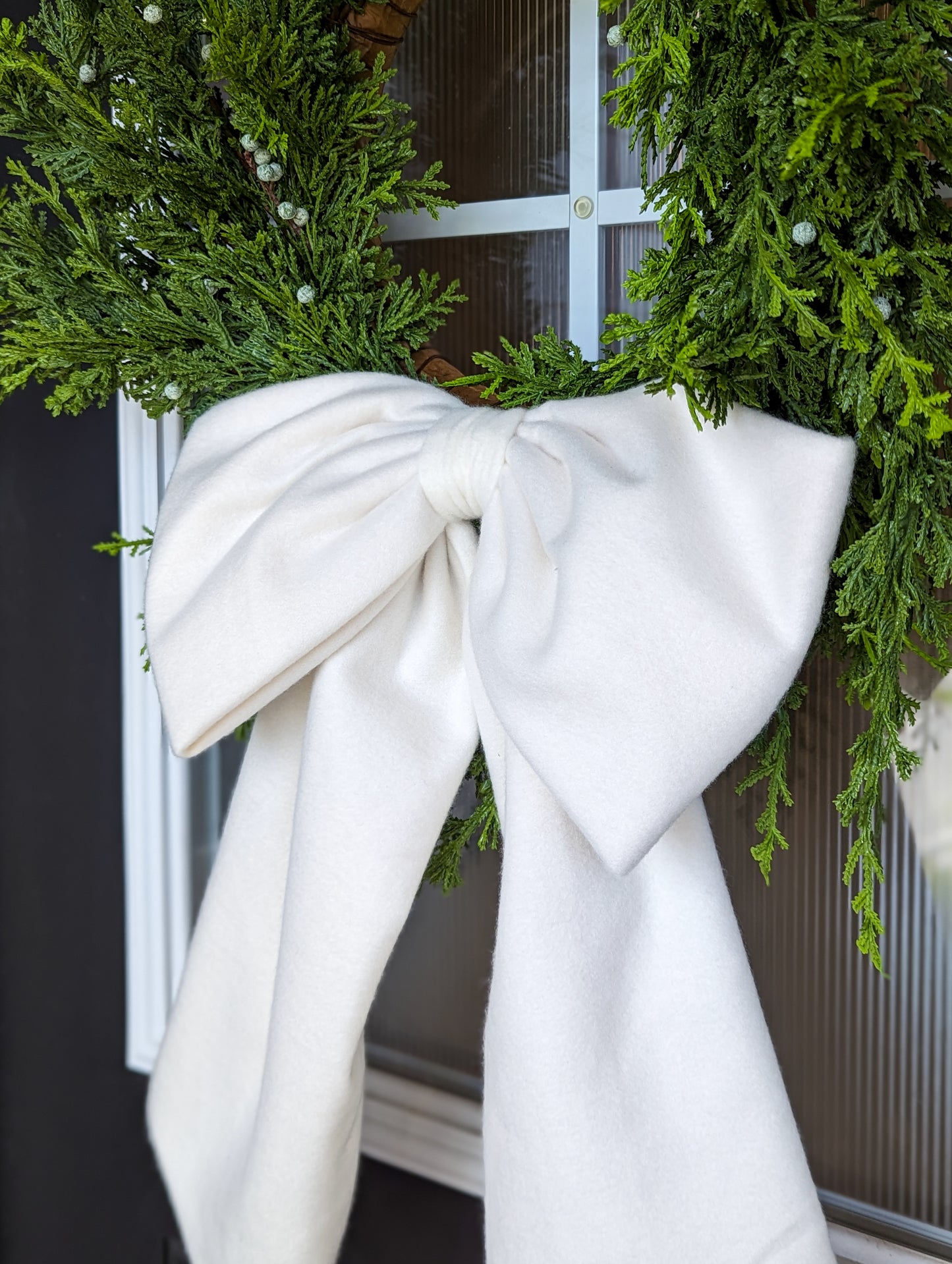 Soft white droopy fleece bow on juniper wreath for holiday home decorating. 