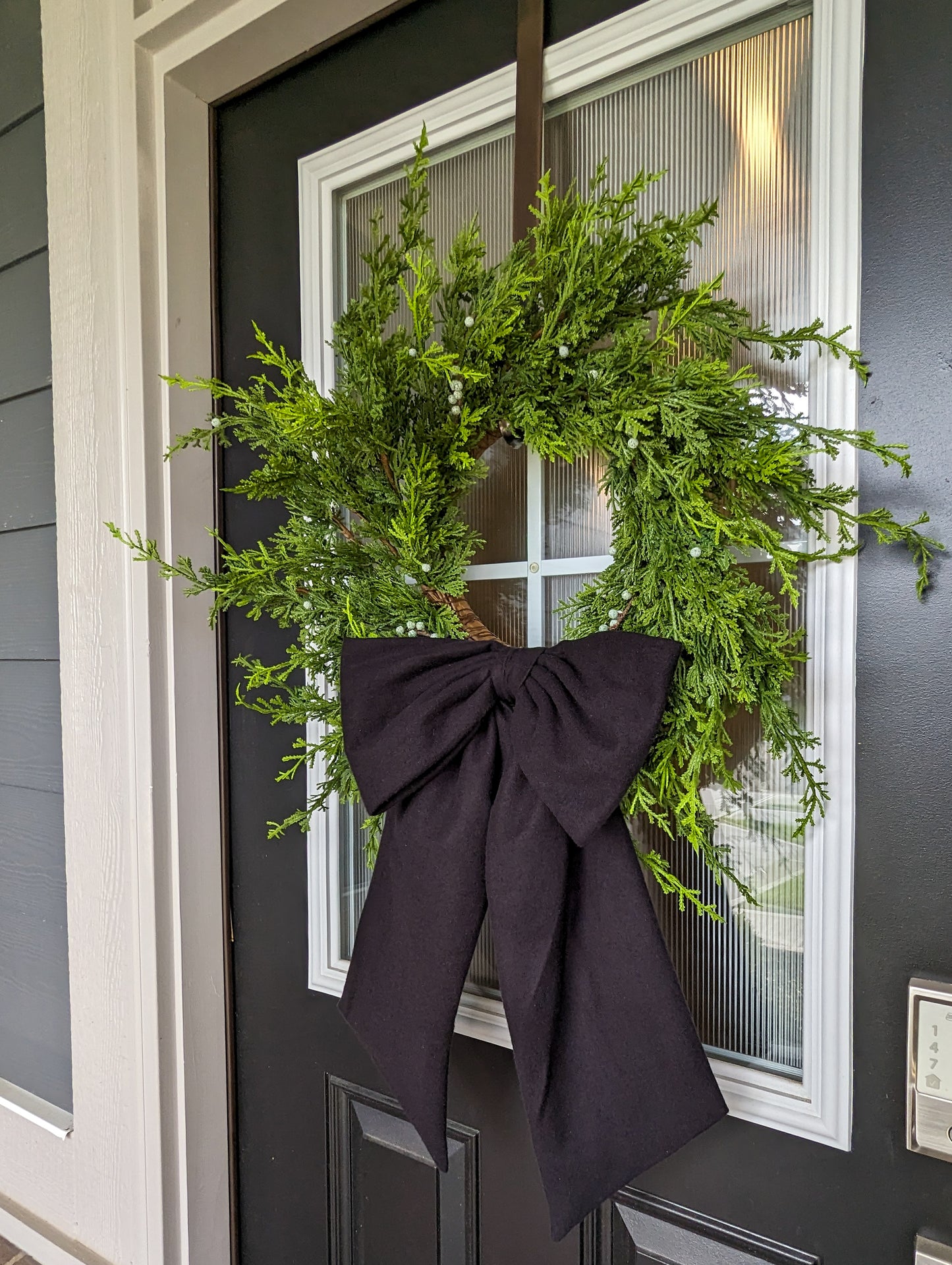 Black droopy fleece bow on juniper wreath for holiday home decorating. 