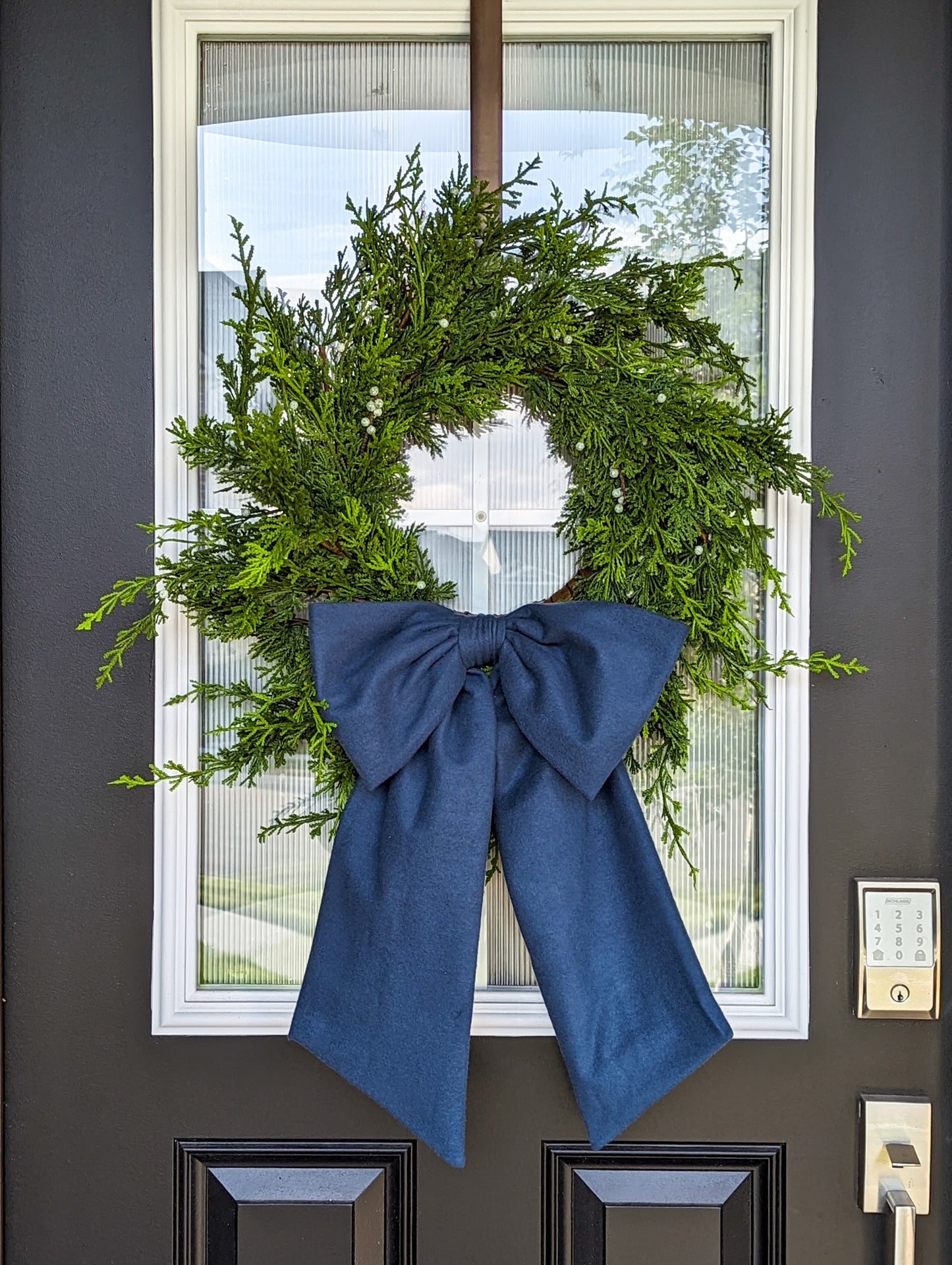 Navy blue droopy fleece bow on juniper wreath for holiday home decorating. 