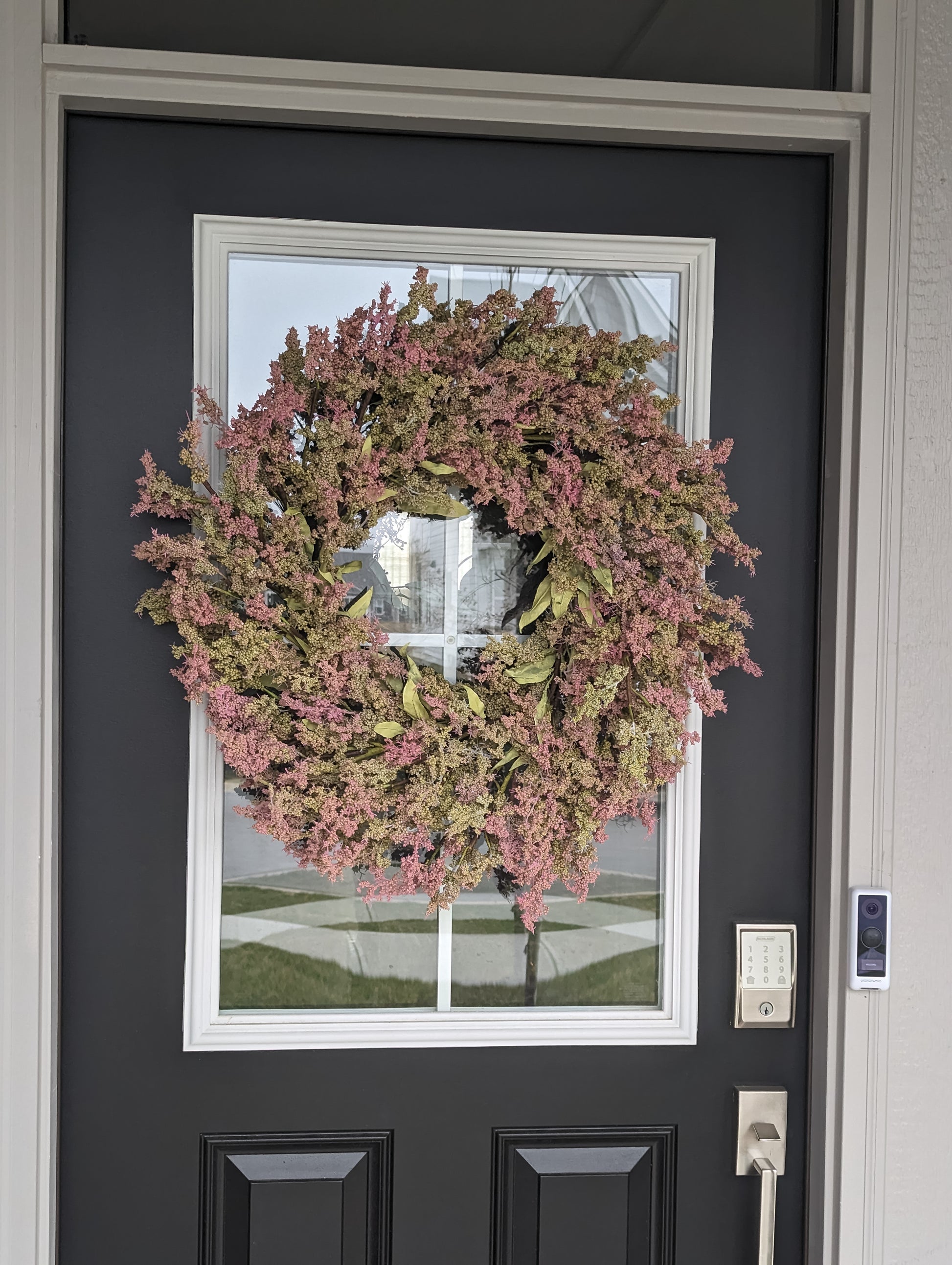 A 26-inch wreath with green leaves, and green and pink bud clusters on a black door. 