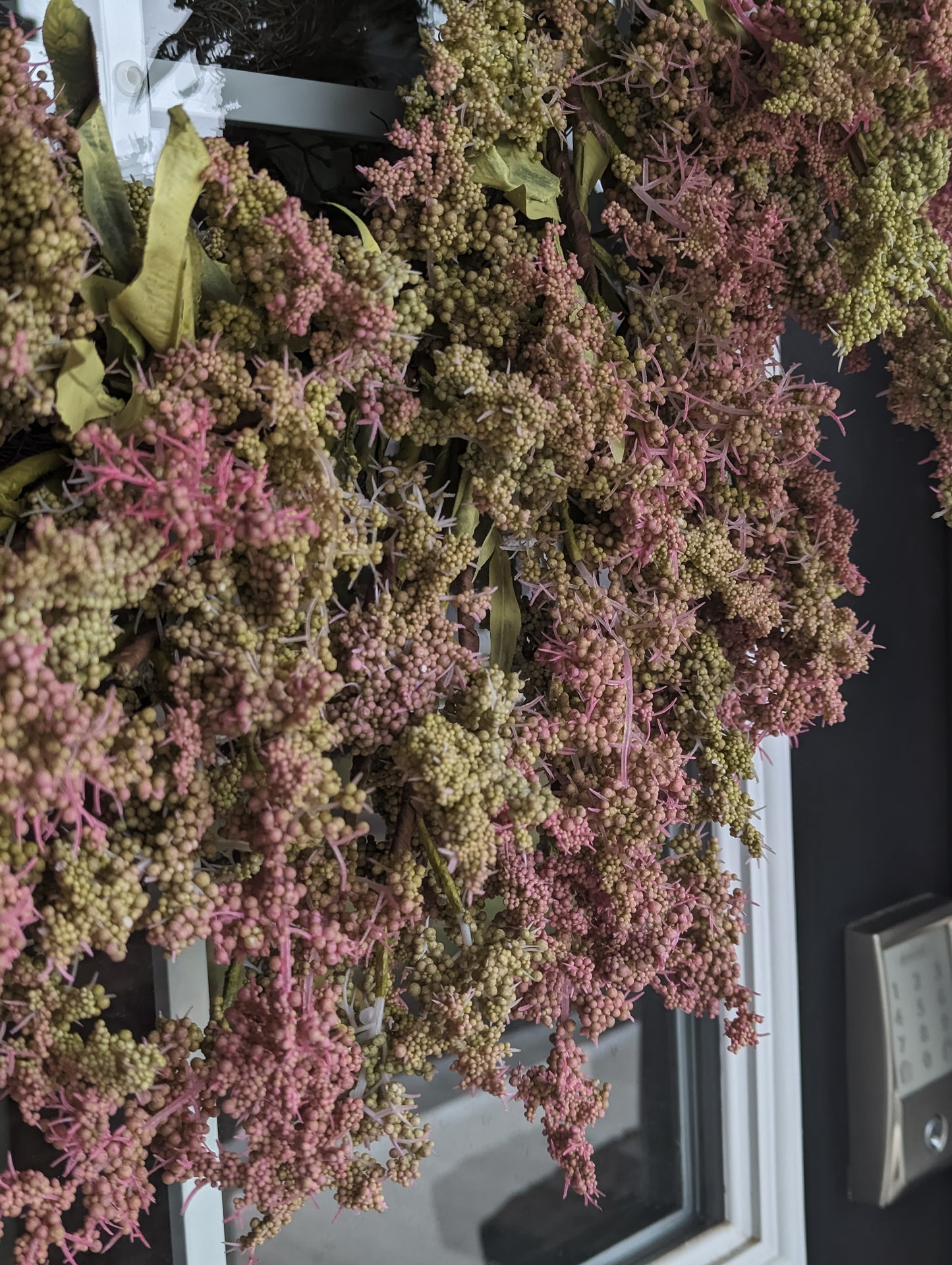 Close up of 26-inch Artificial Wreath, featuring green leaves, and green and pink bud clusters. 