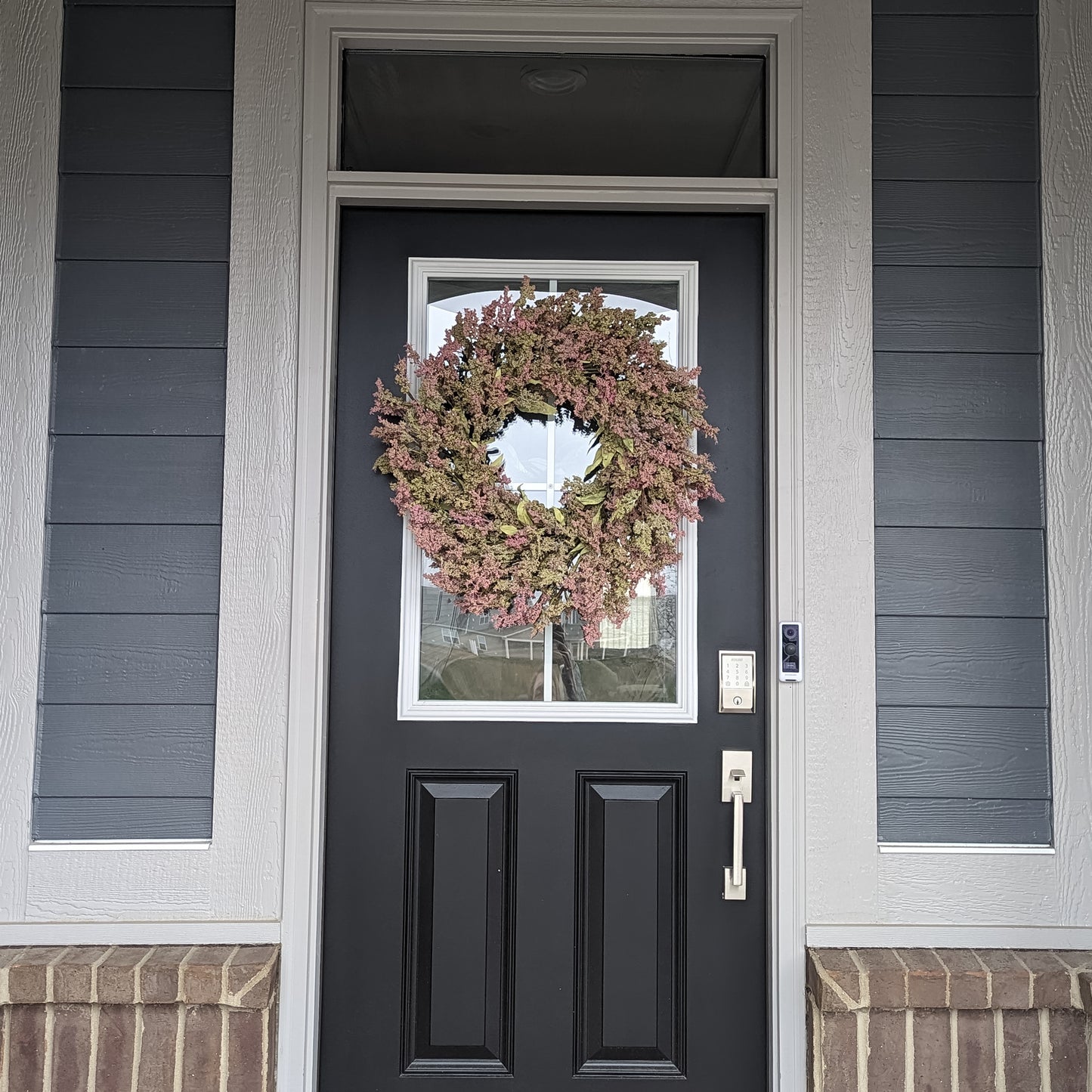 A 26-inch wreath with green leaves, and green and pink bud clusters on a black door. 