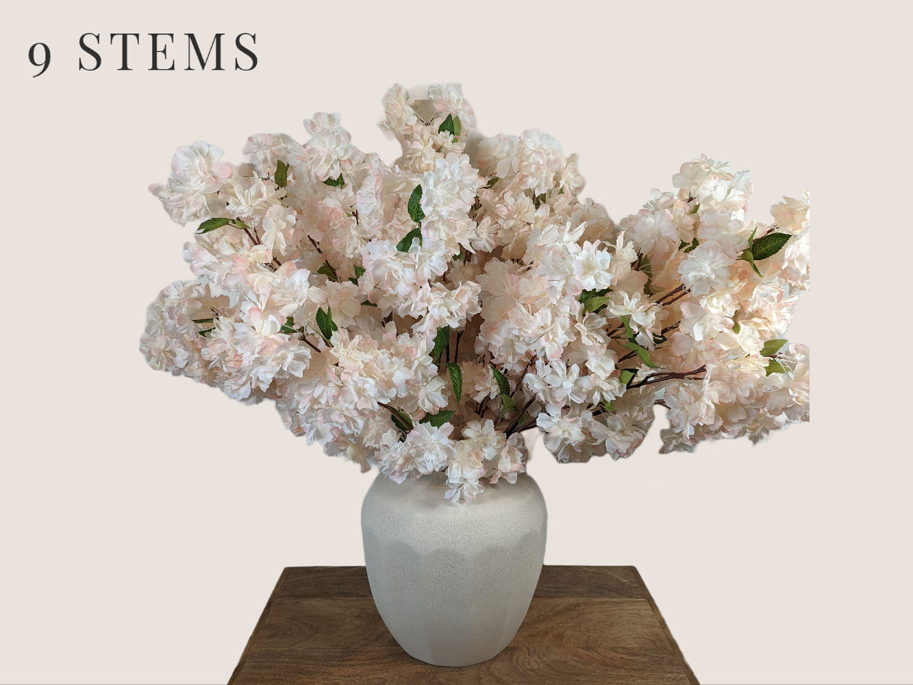 Artificial waterfall cherry blossom stems in soft pink and white, with a brown stem, each stem has 3 branches, with fully, big waterfall blossom blooms. The arrangement includes 9 branches and is displayed in a white vase. The overall height of the arrangement is 38 inches, with 16 inches of stem and 22 inches of branch/flower. The image is set against a neutral beige background.